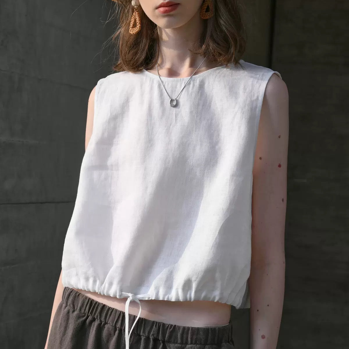 White linen sleeveless crop top with adjustable drawstring hem, minimal chic style